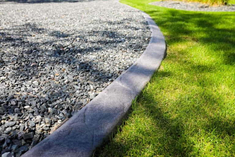 Crushed gravel pathway with concrete edging next to lush green lawn in a landscaped yard.