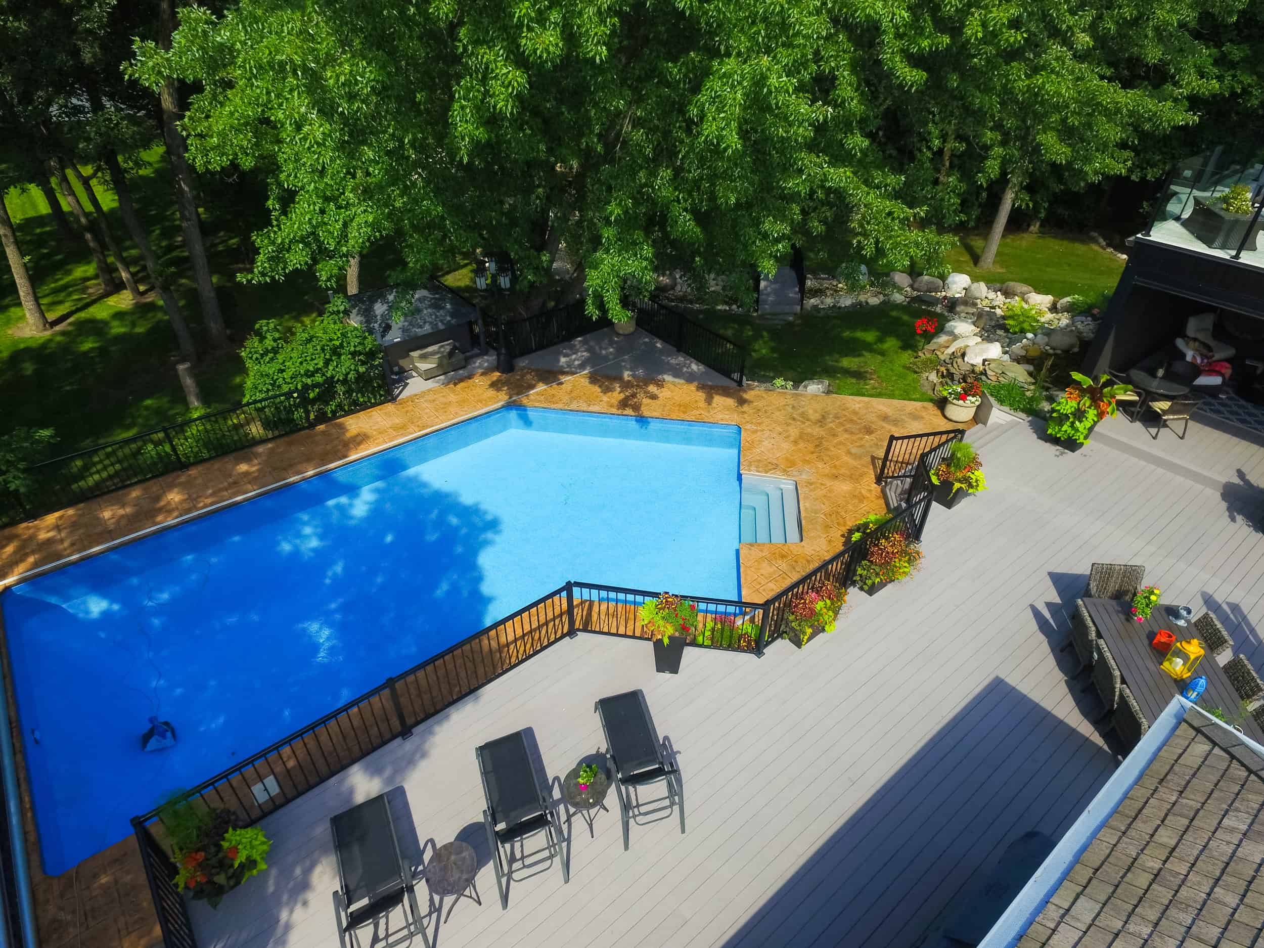 Bright blue swimming pool with a surrounding patio, lush green trees, and a landscaped backyard, highlighting professional lawn and landscape services by Lawn N Order.