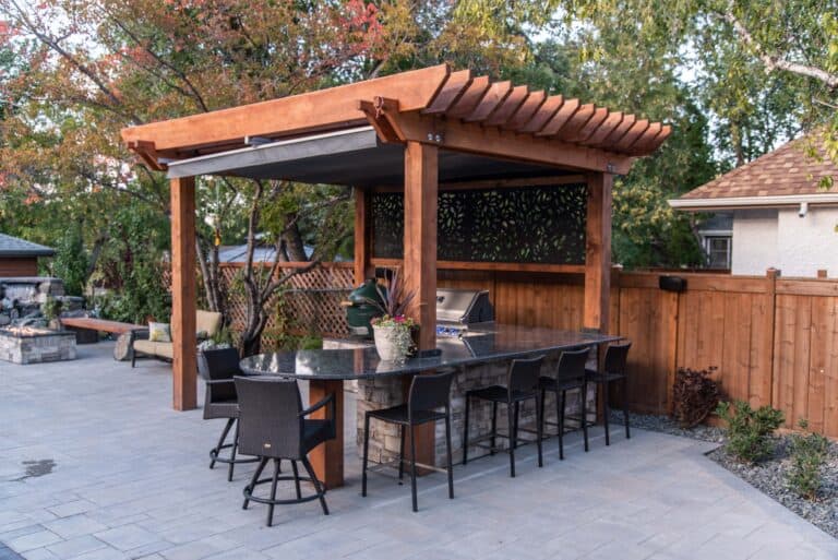 Luxurious outdoor kitchen with a stone countertop, built-in grill, and wooden pergola in a landscaped backyard perfect for entertaining and outdoor cooking.