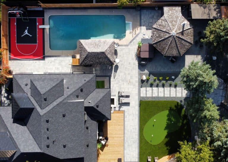 Bright outdoor backyard with swimming pool, basketball court, putting green, patio seating, gazebo, and landscaped garden—ideal for relaxation and entertaining.